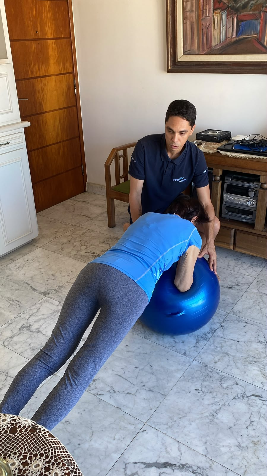 Fisioterapeuta auxiliando paciente em exercício com bola suíça no atendimento domiciliar